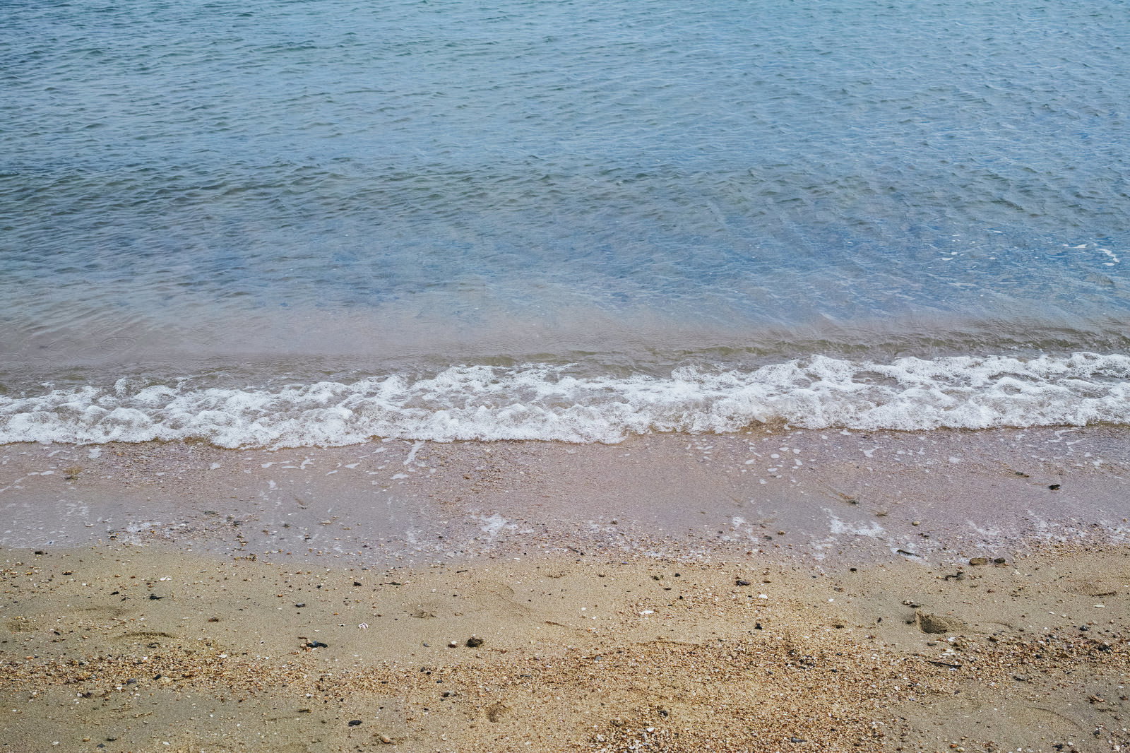 青い海水が砂浜に打ち寄せ、白い泡が波打ち際に広がる様子