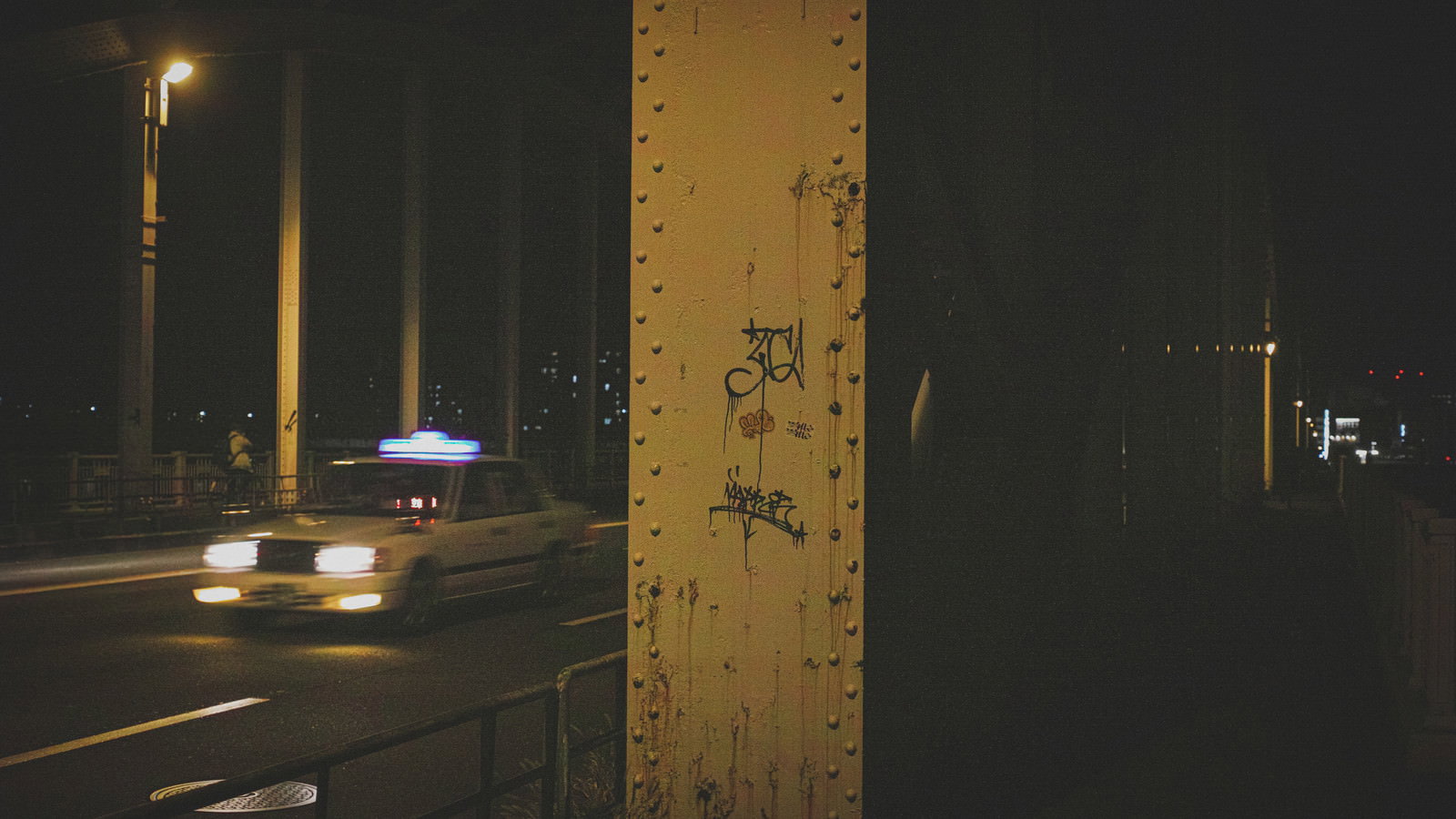 夜の道路脇でアーチ橋の鉄骨コンクリート部分に書かれた落書きが街灯に照らされている様子