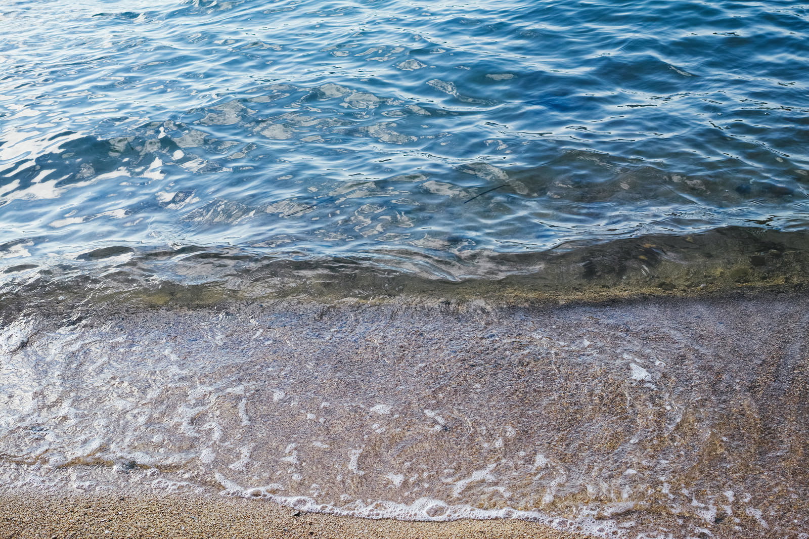 青く透明な海水が白い砂浜に静かに打ち寄せる波打ち際の風景
