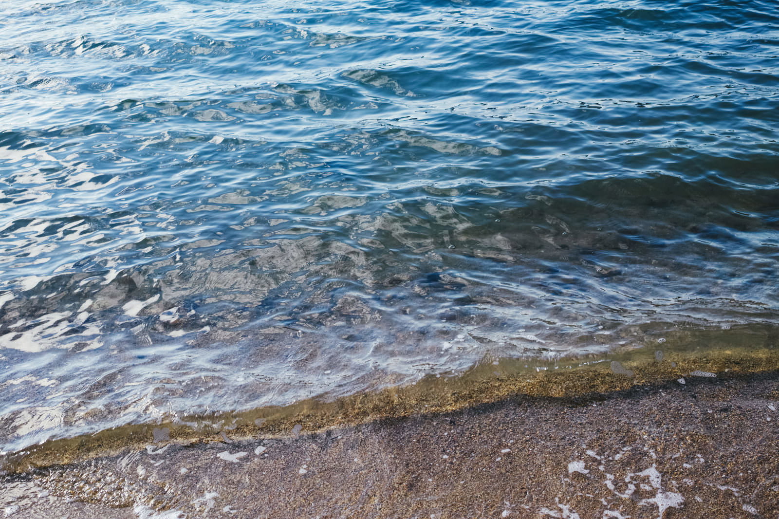 青い海水が砂浜に打ち寄せる波打ち際の様子