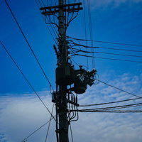 青空と電柱上部に設置された柱上変圧器と送電線の写真