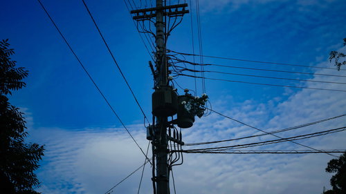 青空と電柱上部に設置された柱上変圧器と送電線