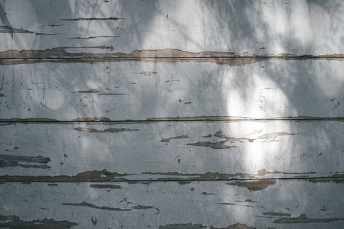 光に照らされる塗装が剥がれた壁の木目テクスチャー