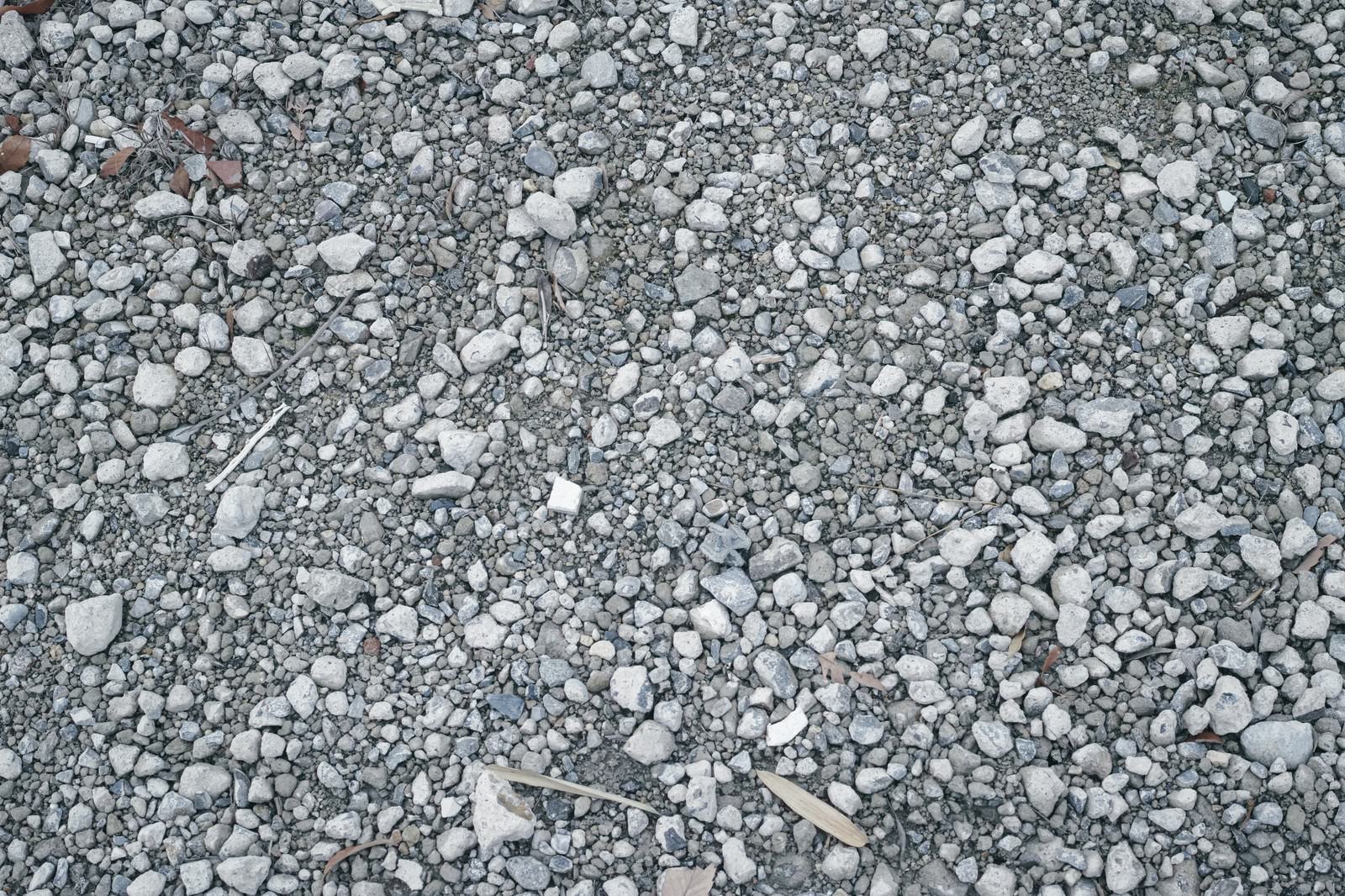 グレー系の小石や砂利が敷き詰められた地面に枯れ葉の破片が散らばるテクスチャー
