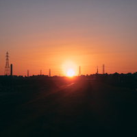 河川敷に昇る日の出の瞬間を彩る送電塔と工業地帯のシルエットの写真