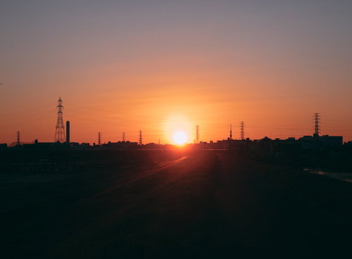 河川敷に昇る日の出の瞬間を彩る送電塔と工業地帯のシルエット