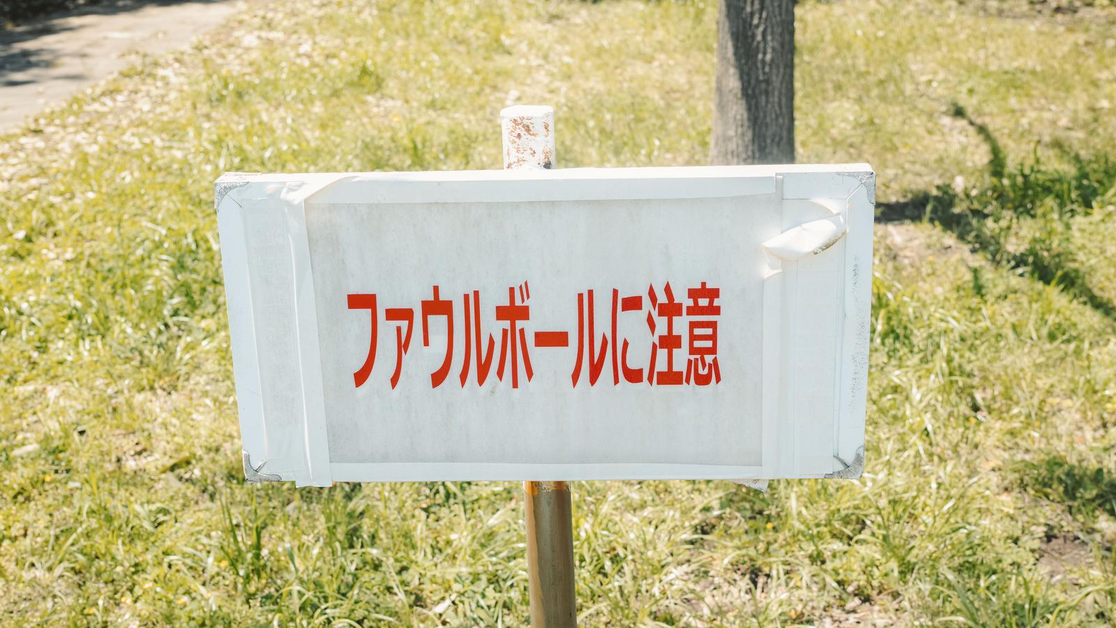 野球場の柱に取り付けられた「ファウルボールに注意」という赤い日本語の警告看板