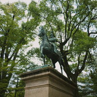 有栖川宮熾仁親王の騎馬銅像と新緑に囲まれた広場の写真