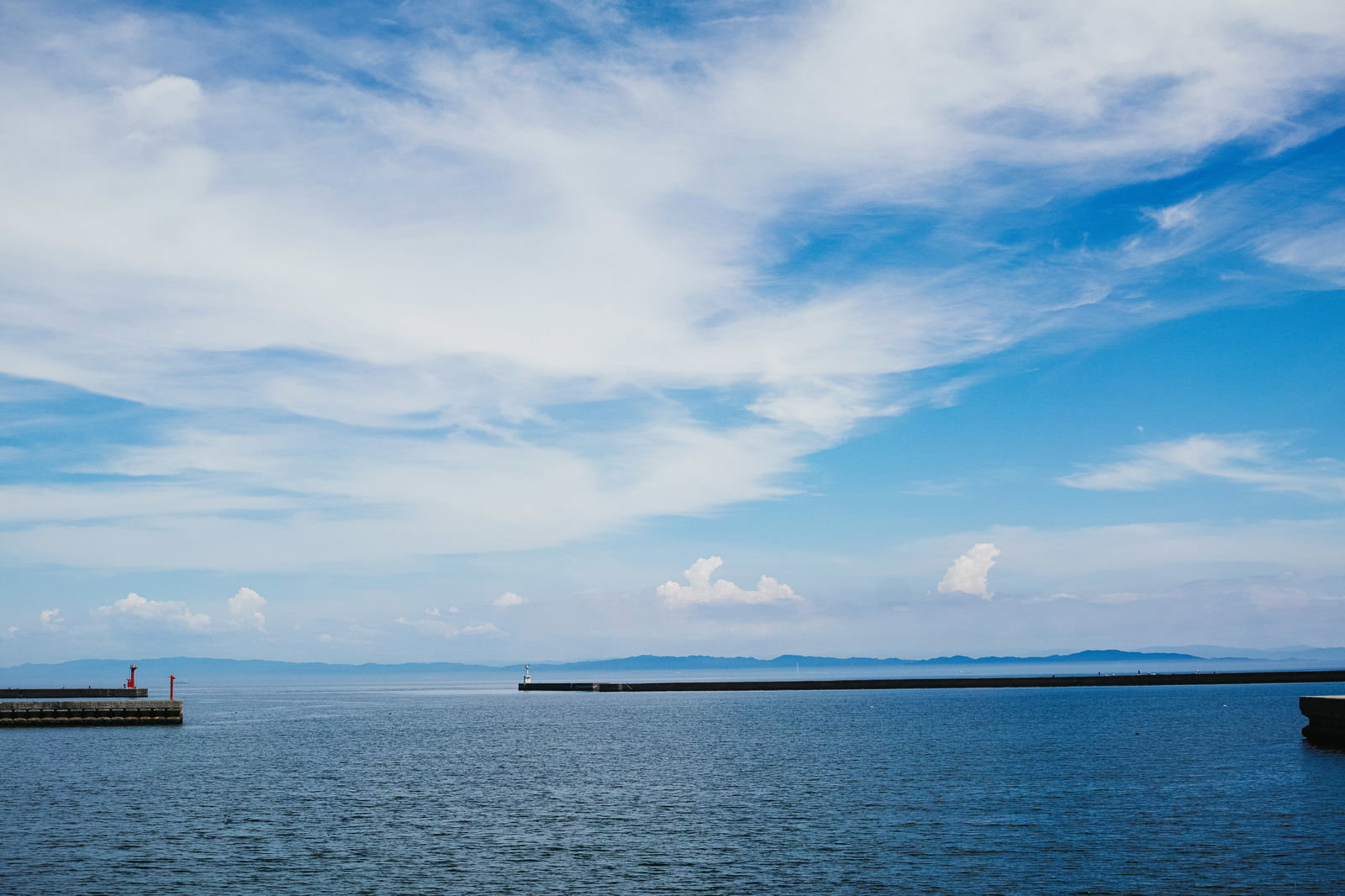 青空と雲の下、穏やかな瀬戸内海に延びる堤防の風景