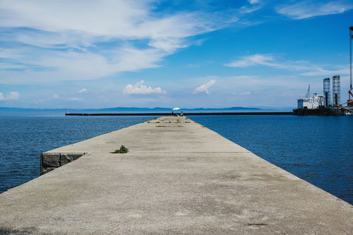 瀬戸内海の堤防の先端で釣りをする人と港の風景