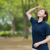 森林の公園で木漏れ日を見上げる紺色制服の介護士の写真