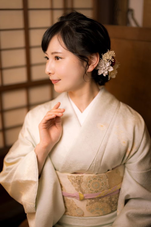 白い着物に金色の帯を締めた女将の横顔、和室で微笑む