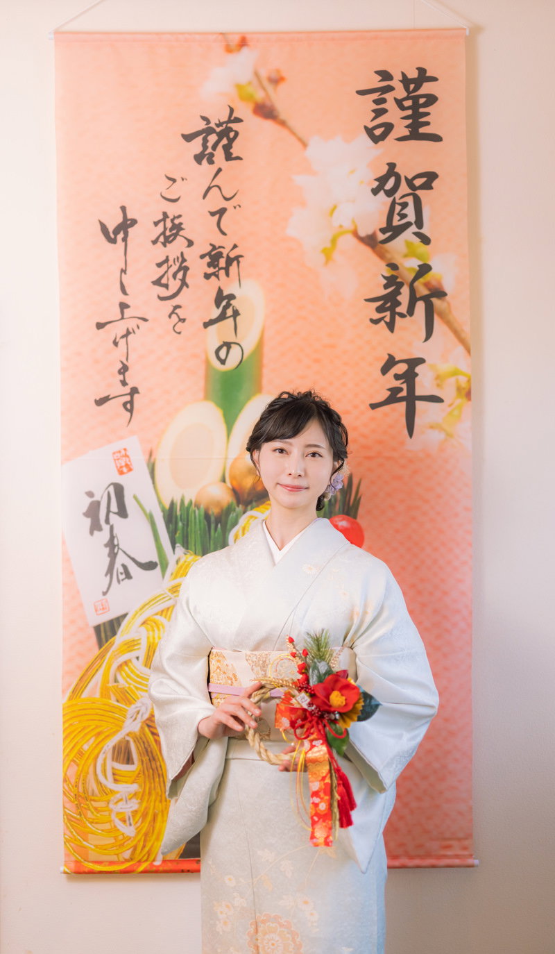 謹賀新年の掛け軸の前で正月飾りを持つ白い着物姿の女性［モデル：yumiko］