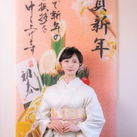 謹賀新年幕の前に立つ白い着物姿の女性の写真