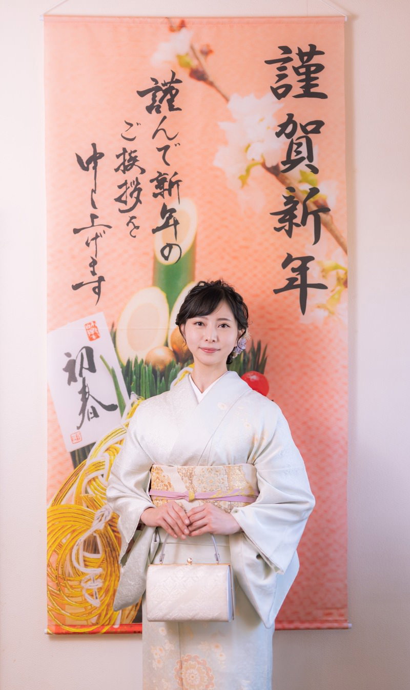 謹賀新年と書かれた幕の前に立つ白い着物を着た女性［モデル：yumiko］