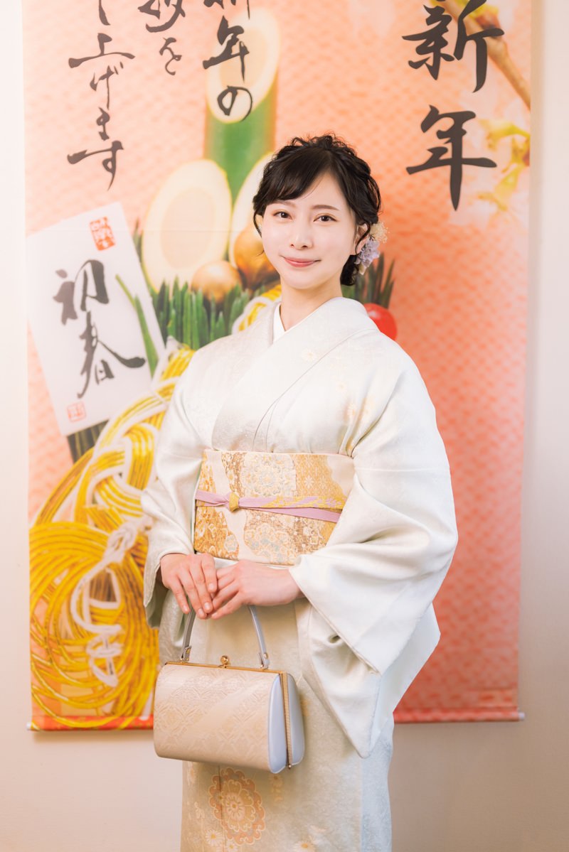 薄いピンク色の着物を着た女性が新年の装飾背景の前に立つ［モデル：yumiko］