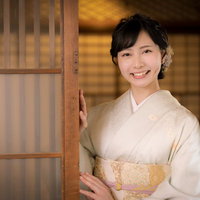 淡いベージュの着物を着て笑顔でお見送りをする女性の写真