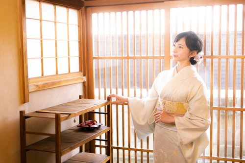 光が差し込む木造の玄関で着物姿の女性が佇む