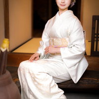 玄関で正座する白い着物の女将の写真