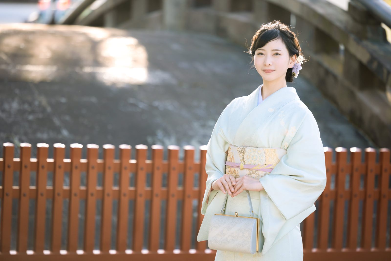 淡い着物を着た女性が境内の木製柵の前でポーズを取っている様子［モデル：yumiko］