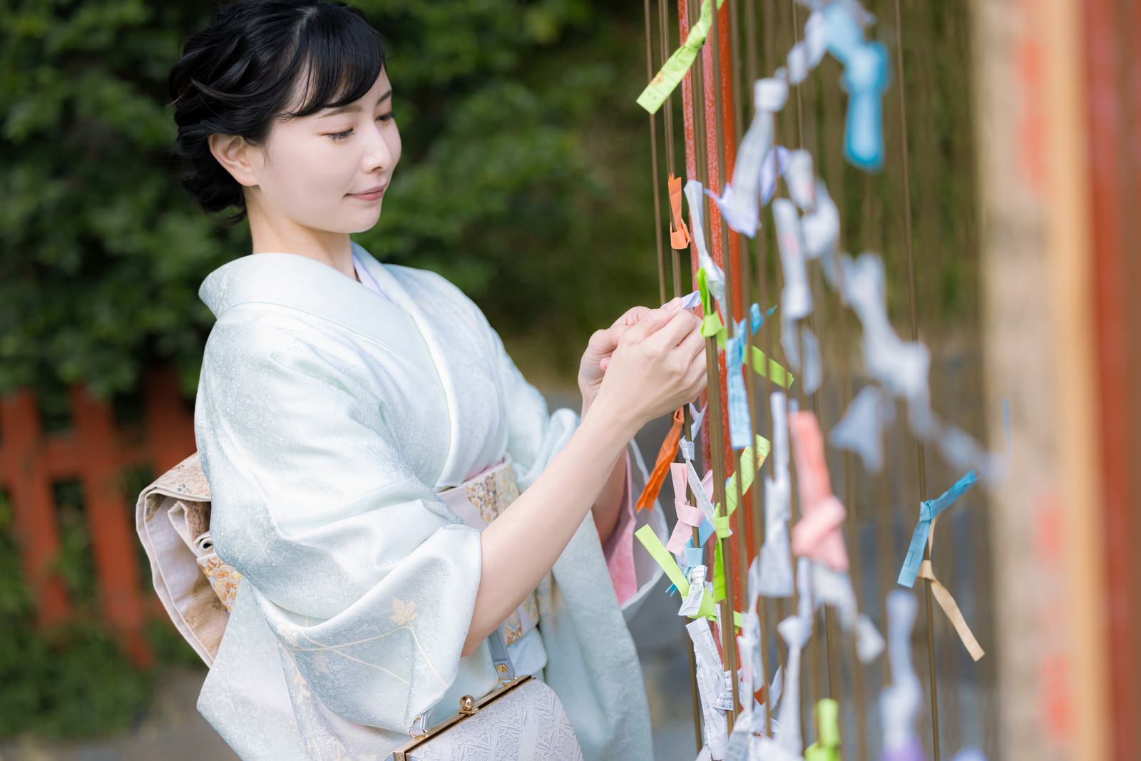 神社の境内で白い着物を着た女性がおみくじを結んでいる［モデル：yumiko］
