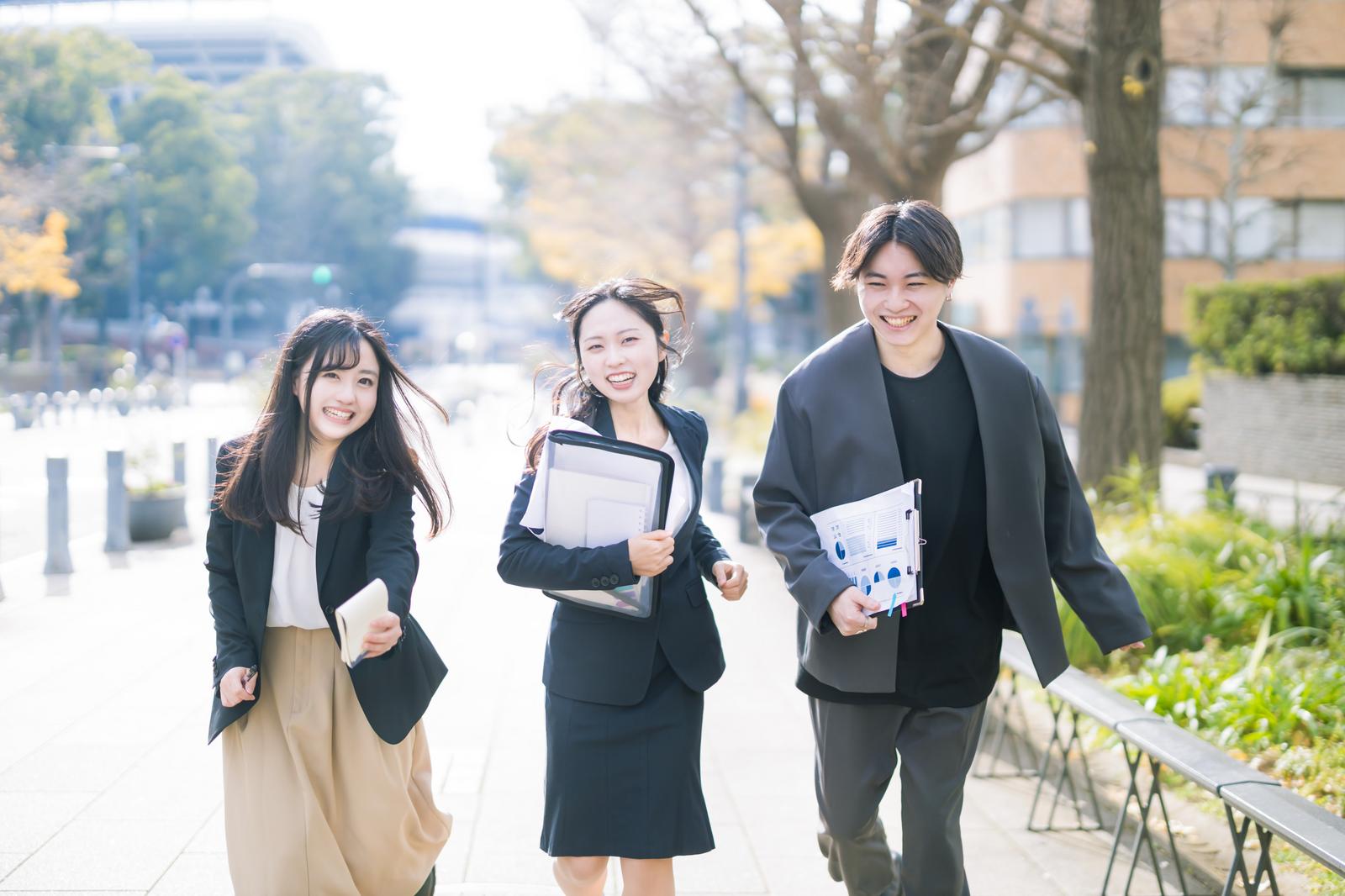 資料を持って屋外を歩くスーツ姿の男女3人［モデル：吉屋ゆり SHUN 河村友歌］