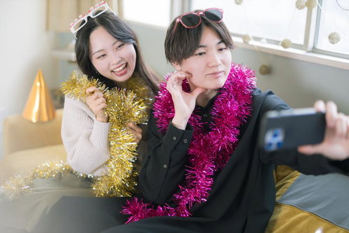 仲良しカップルがスマホで自撮りなう、パーティーハットとテープル巻きで盛り上がり