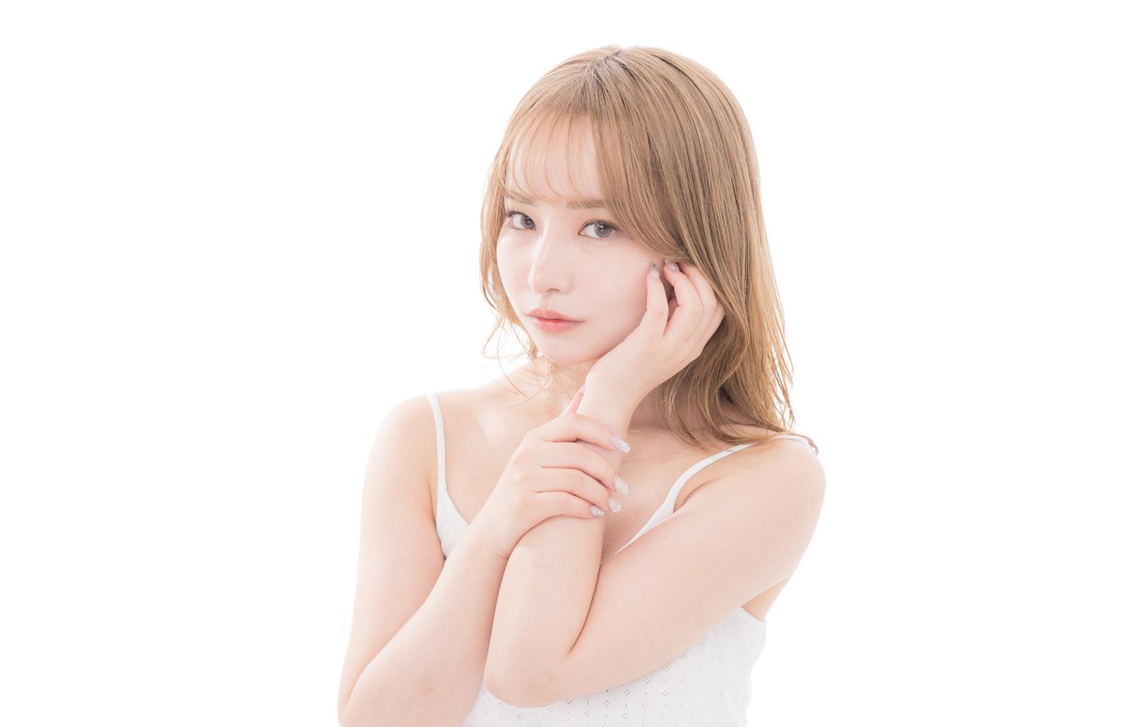 白いキャミソール姿で頬に手を当てる女性、ナチュラルメイクと透明感のある肌［モデル：yuria］