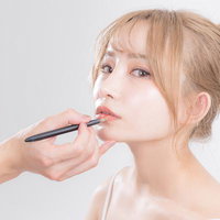 リップメイクを仕上げる女性の横顔、リップペンシルでメイク施術中の写真