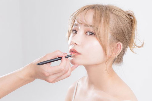 リップメイクを仕上げる女性の横顔、リップペンシルでメイク施術中