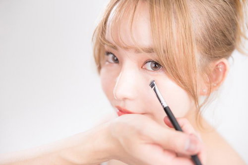 アイブロウブラシを使用したアイメイクの女性