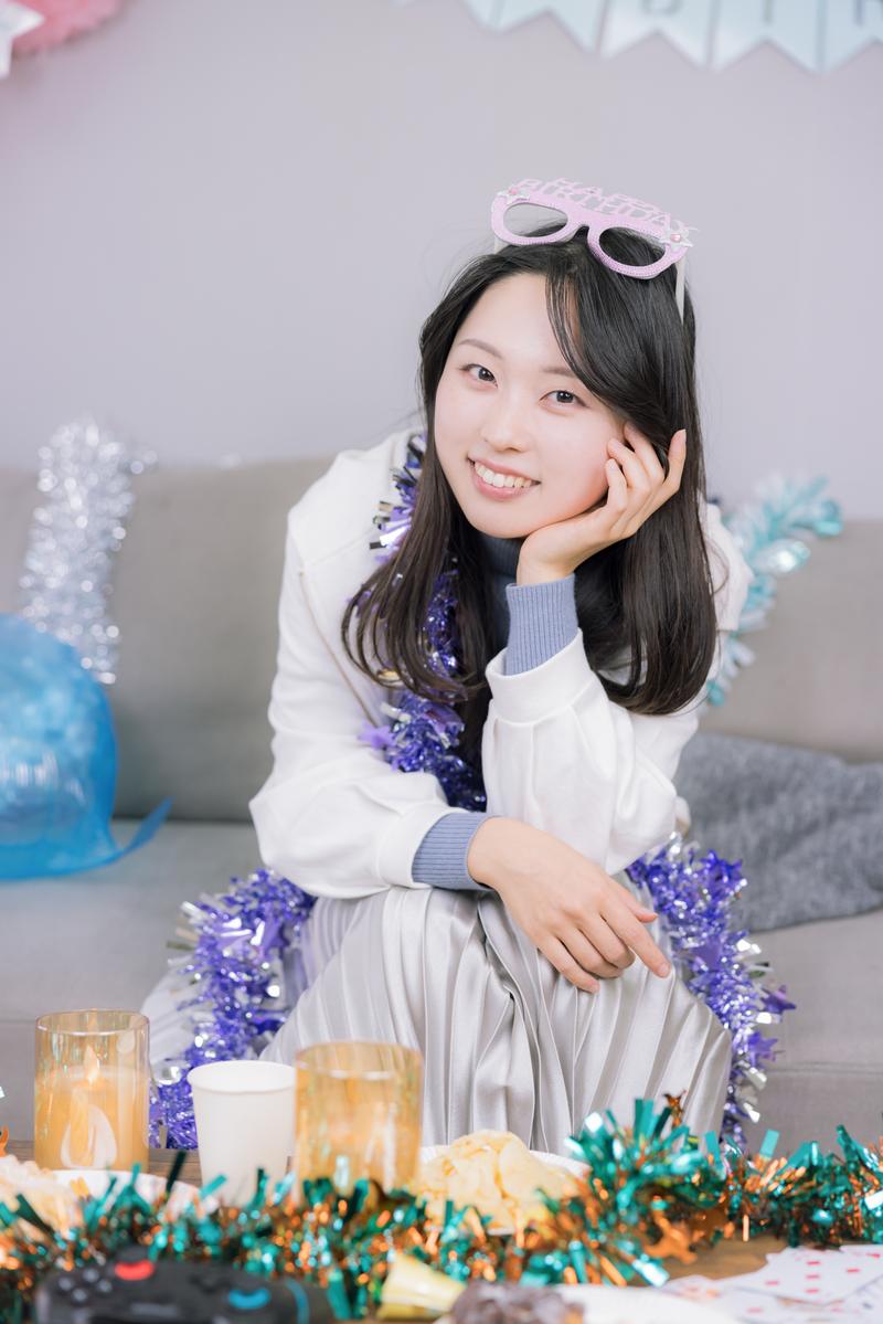 パーティー装飾に囲まれた笑顔の女性がソファーに座っている［モデル：吉屋ゆり］
