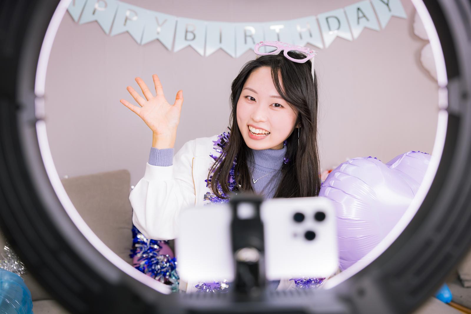 リングライト配信でスパチャをせがぐ女性、背景に誕生日装飾［モデル：吉屋ゆり］