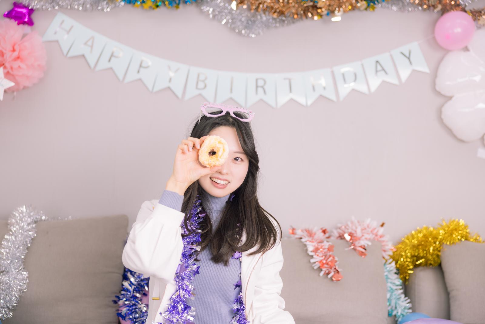 HAPPY BIRTHDAYのガーランドの前でドーナッツを持って笑う女性［モデル：吉屋ゆり］