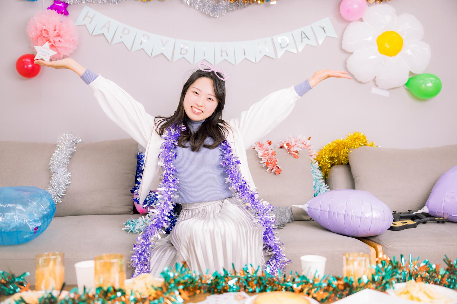 バースデイパーティーの装飾に囲まれたソファーに座る笑顔の女性［モデル：吉屋ゆり］