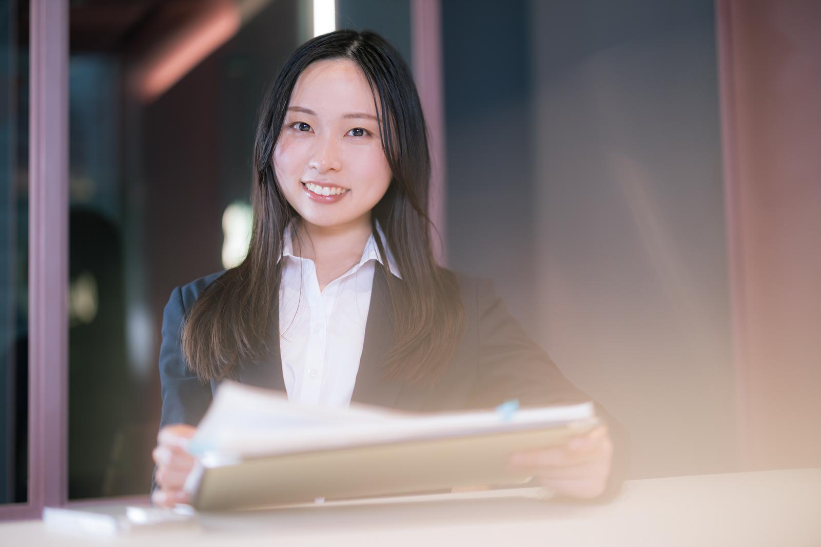 会議室で書類を手に笑顔を見せるスーツ姿の女性社員［モデル：吉屋ゆり］