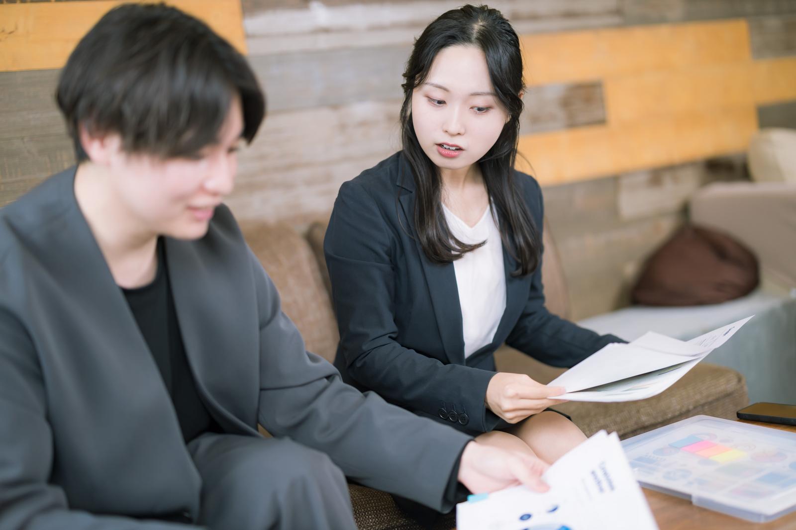 紙の資料を確認する男女がソファーに座って打ち合わせをしている［モデル：吉屋ゆり SHUN］