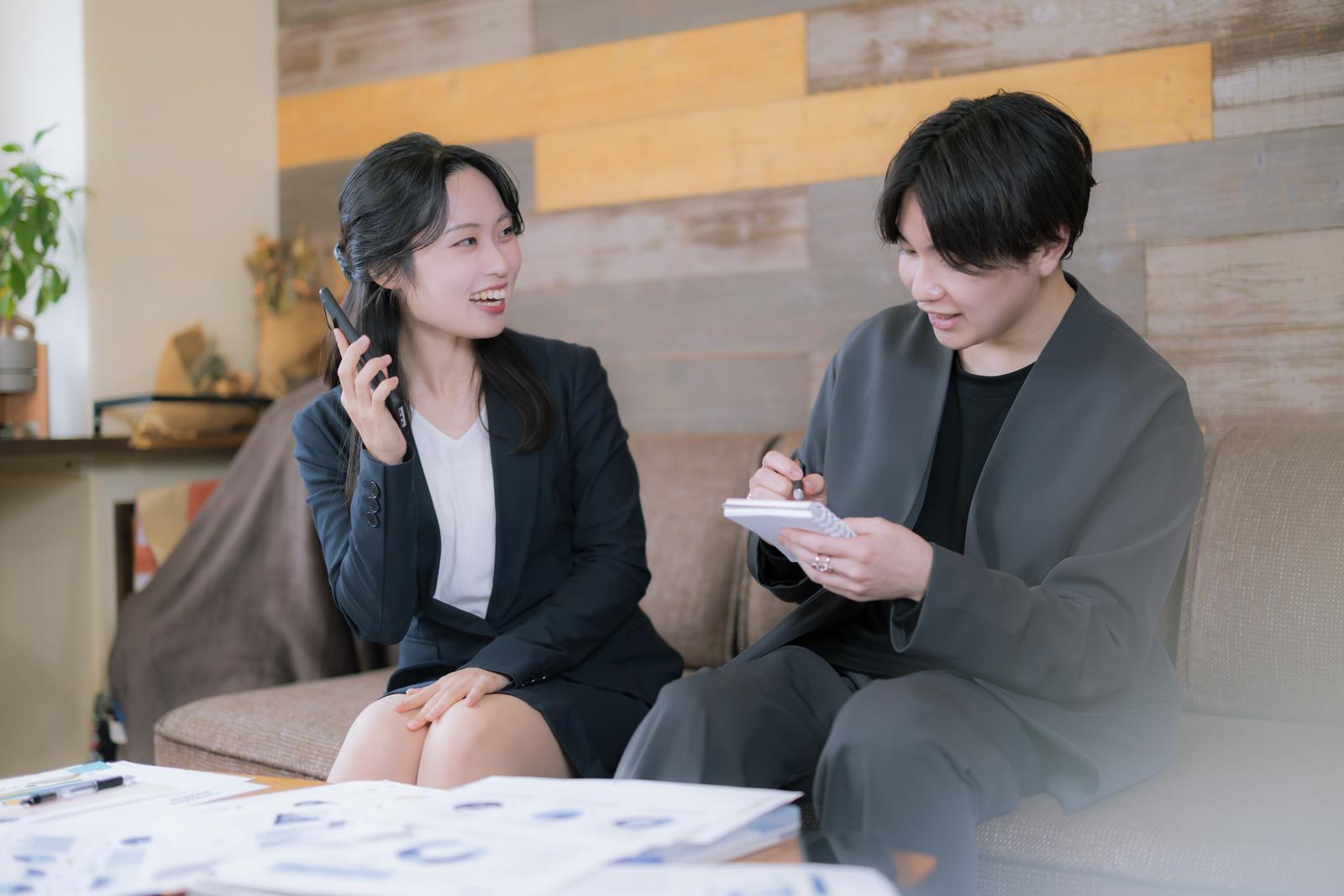 会議室でメモを取る男性と電話を持つ笑顔の女性社員［モデル：SHUN 吉屋ゆり］