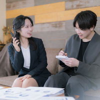 電話の内容をメモる部下と商談がまとまって笑顔がこぼれる若手社員と上司の写真