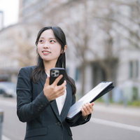 スマホで資料をチェックするスーツ姿の女性の写真