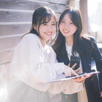 資料とスマホを持って笑顔で提案する女性社員ふたりの写真