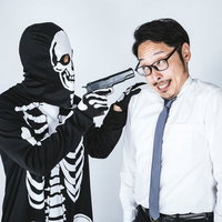 危機的状況に怯える会社員と拳銃を構える骸骨の仮装人物の写真