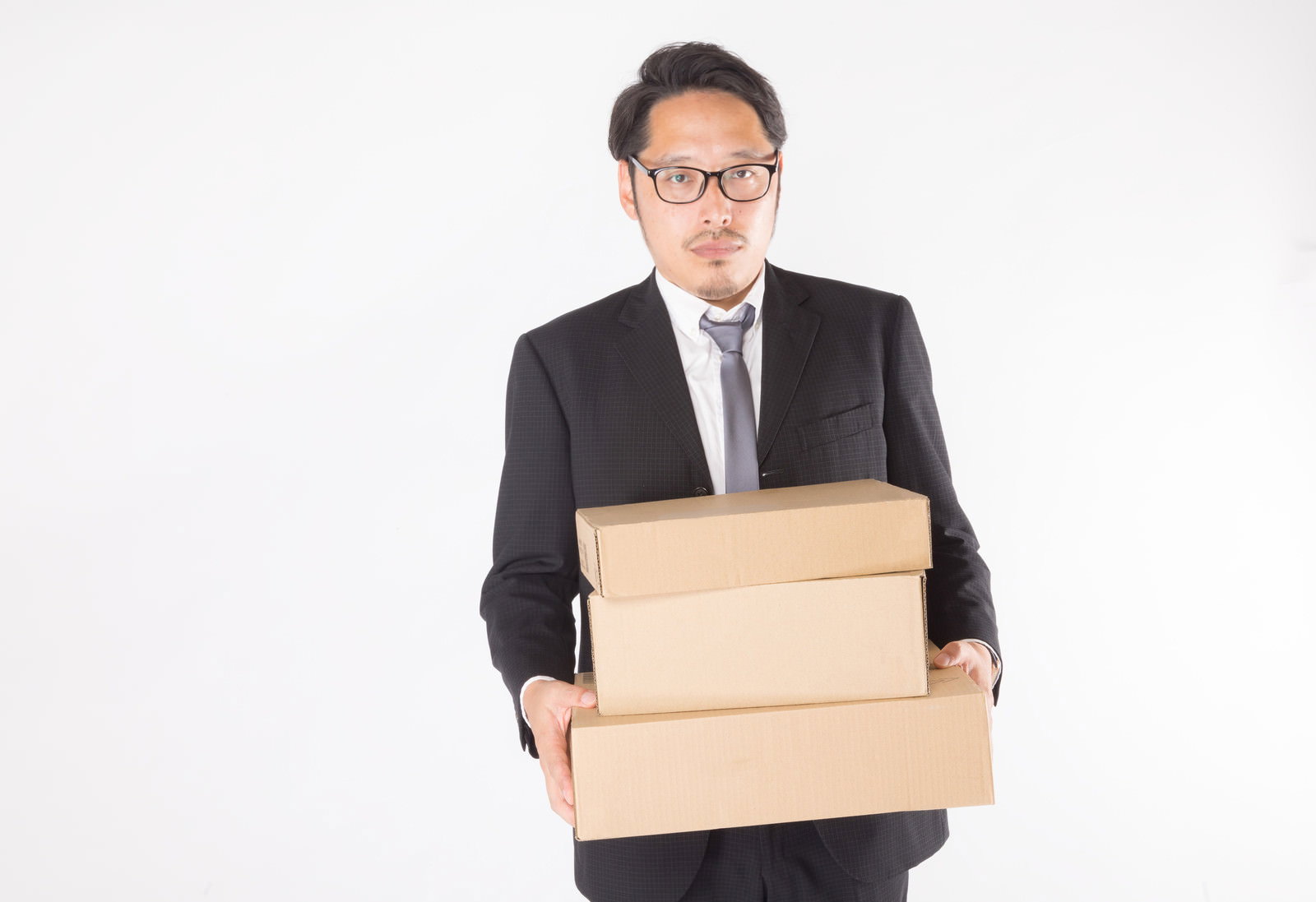 黒いスーツを着た眼鏡の男性がダンボール箱を複数抱えて運んでいる［モデル：ゆうせい］