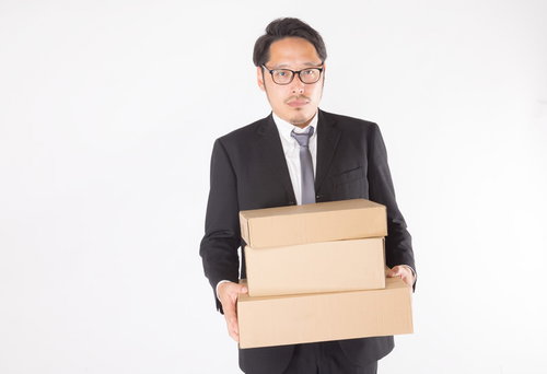届いたダンボール箱を両手で抱えて運ぶ眼鏡の総務部長