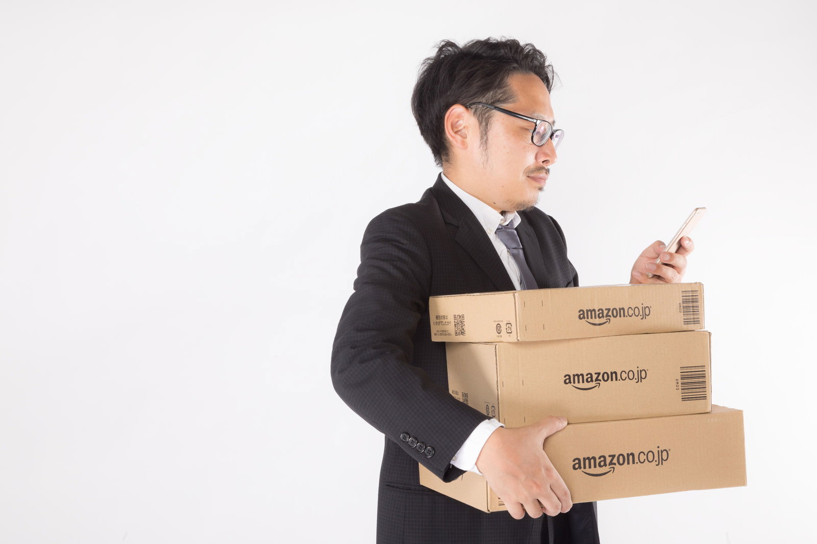 複数のダンボール箱を抱えてスマートフォンを見るスーツ姿の男性［モデル：ゆうせい］