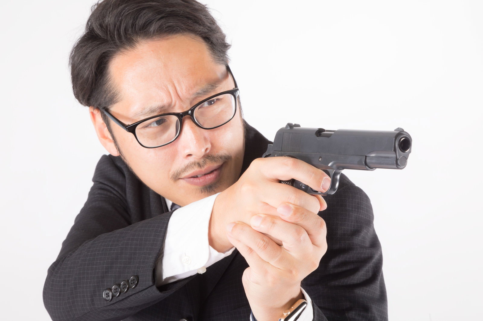 黒いスーツを着た眼鏡の男性が両手で拳銃を構えている様子［モデル：ゆうせい］
