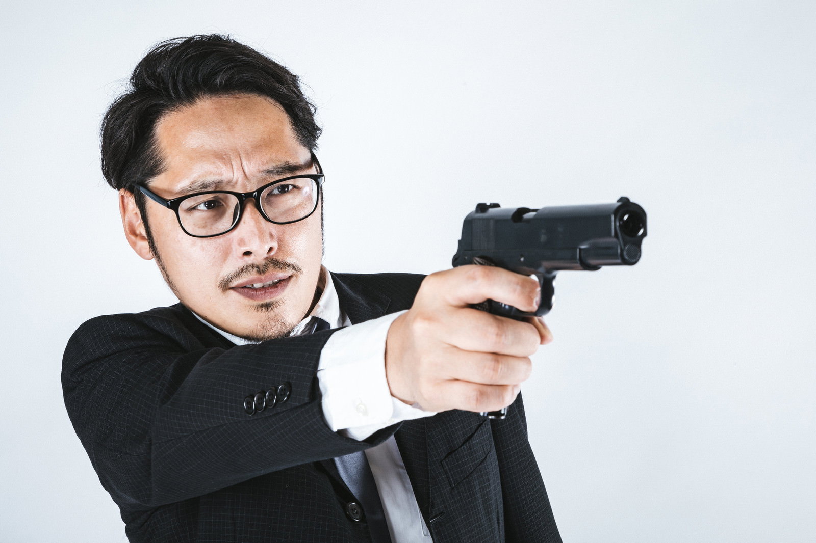 黒いスーツを着た眼鏡の男性が両手で拳銃を構えているポーズ［モデル：ゆうせい］