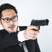 ガン・フーアクション風に拳銃を構えるスーツ姿の眼鏡の男性の写真
