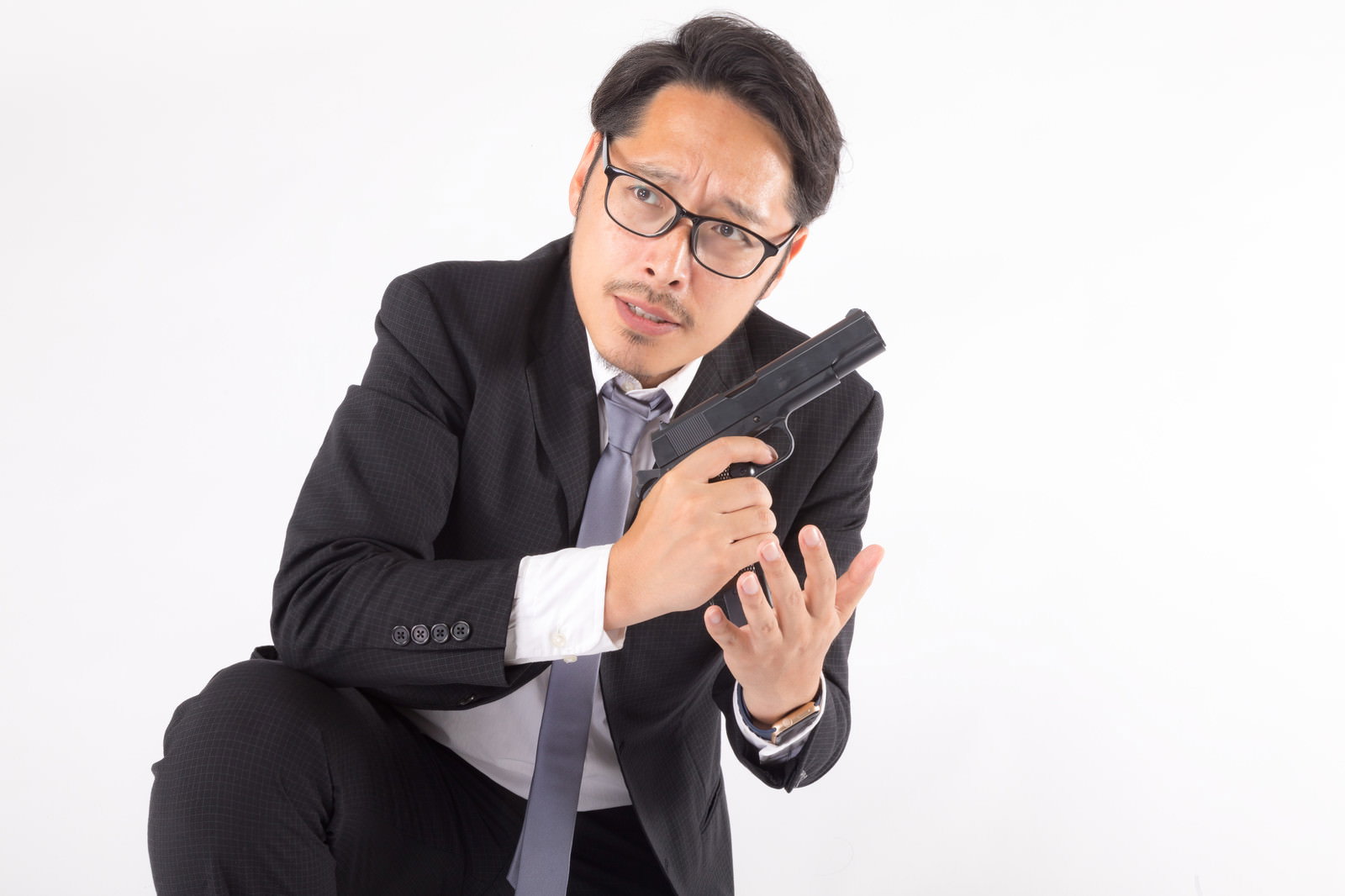 黒いスーツを着た眼鏡の男性が拳銃に弾倉を装填している［モデル：ゆうせい］