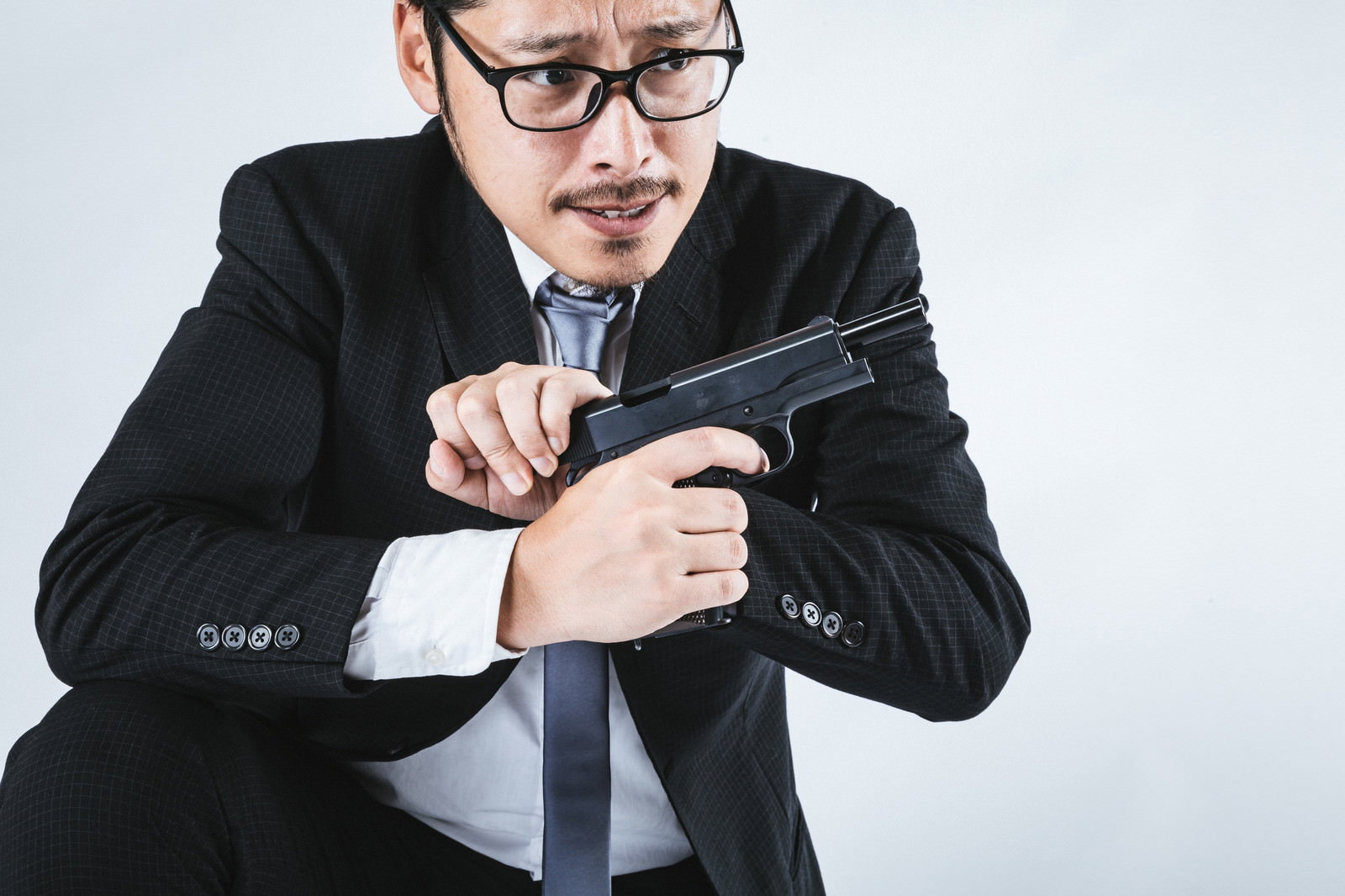 黒いスーツを着た眼鏡の男性が拳銃をリロードしている様子［モデル：ゆうせい］